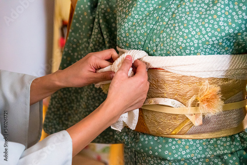 Japanese, Okinawan woman's hands tying obiage cloth around the obi during traditional kimono dressing photo