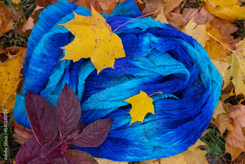 Handmade women's neckerchief on yellow autumn leaves. Handmade women's shawl, deep beautiful shades of blue
