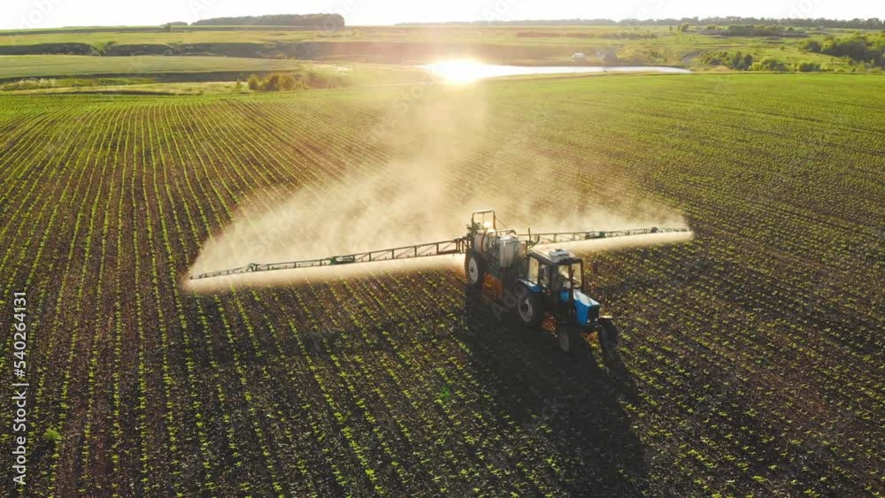 Aerial view of working farming tractor spraying on field with sprayer water or herbicides and pesticides against diseases and insects. Nature landscape of rivers, reservoirs. Agricultural industry.