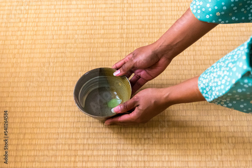 African American woman guest hands serving matcha tea in chawan tea bowl to Japanese woman, tea master, Sen Rikyu photo