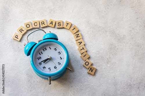 Procrastination text with blue alarm clock on concrete background. Time management concept. photo