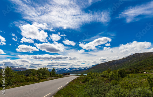 Scandinavian Summer Afternoon With Road And Snow Capped Mountains In The Distance Under Blue Skies In Norway June 2019