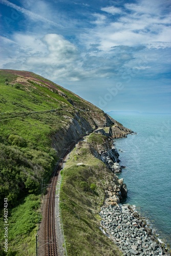Fotografija Vertical shot of the rocky green cliffs with a trail near water near Bray and Gr