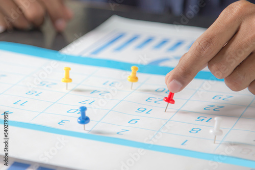 Hand choose rad pin on business desk calendar with office equipment concept of event planner or personal organization reminder and schedule or planning.