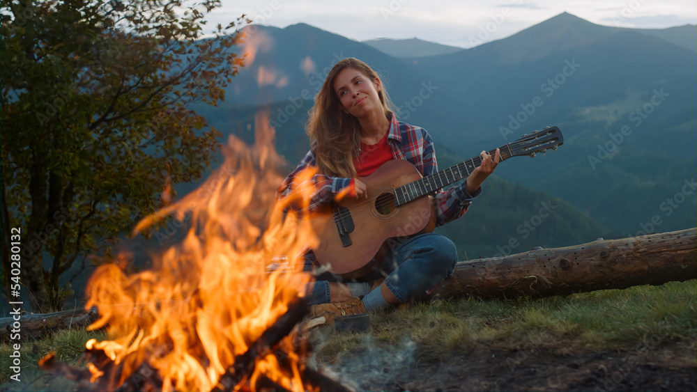 Smiling woman play guitar in mountains. Happy camper relax on green hill forest.