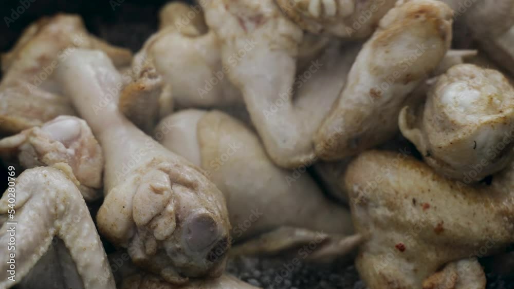 The cook prepares chicken - legs and wings in a cauldron in the open air. Close-up. The cook prepares chicken - legs and wings in a cauldron in the open air. Close-up.