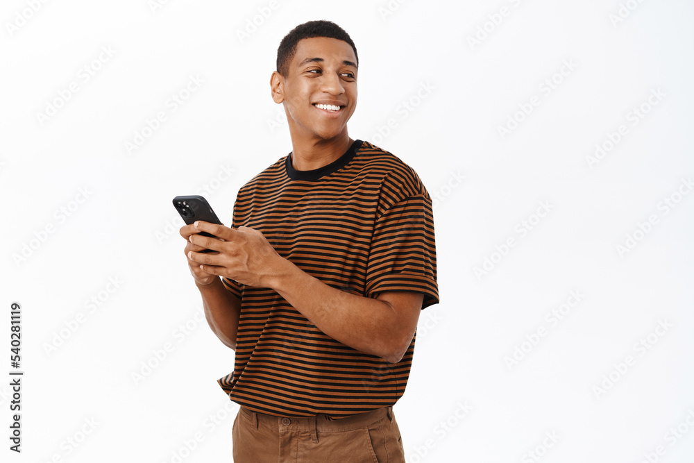 Mobile technology concept. Smiling african american man using his smartphone, holding phone and looking happy, texting in application, white background Mobile technology concept. Smiling african american man using his smartphone, holding phone and looking happy, texting in application, white background