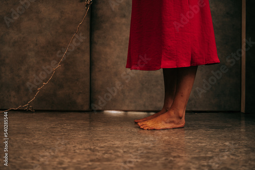 The legs of a woman wearing a red dress were bound by the assailant standing in a scary room. Victims of violence, human trafficking, stop abusing violence, kidnapping, and copy space. photo