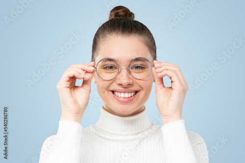 Woman holding glasses she wearing, smiling at camera, satisfied with good eyesight