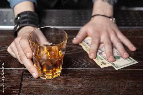 Bartender is holding out a glass of whiskey and taking the money.
