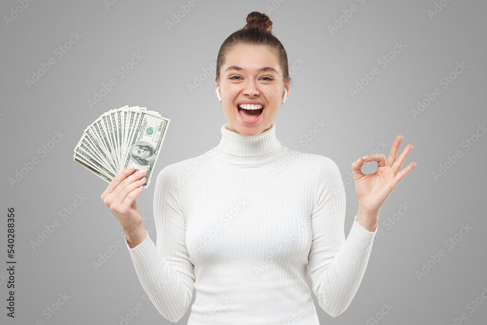 Woman excited because of her victory in lottery, holding fan of 100 dollar banknotes, showing ok Woman excited because of her victory in lottery, holding fan of 100 dollar banknotes, showing ok