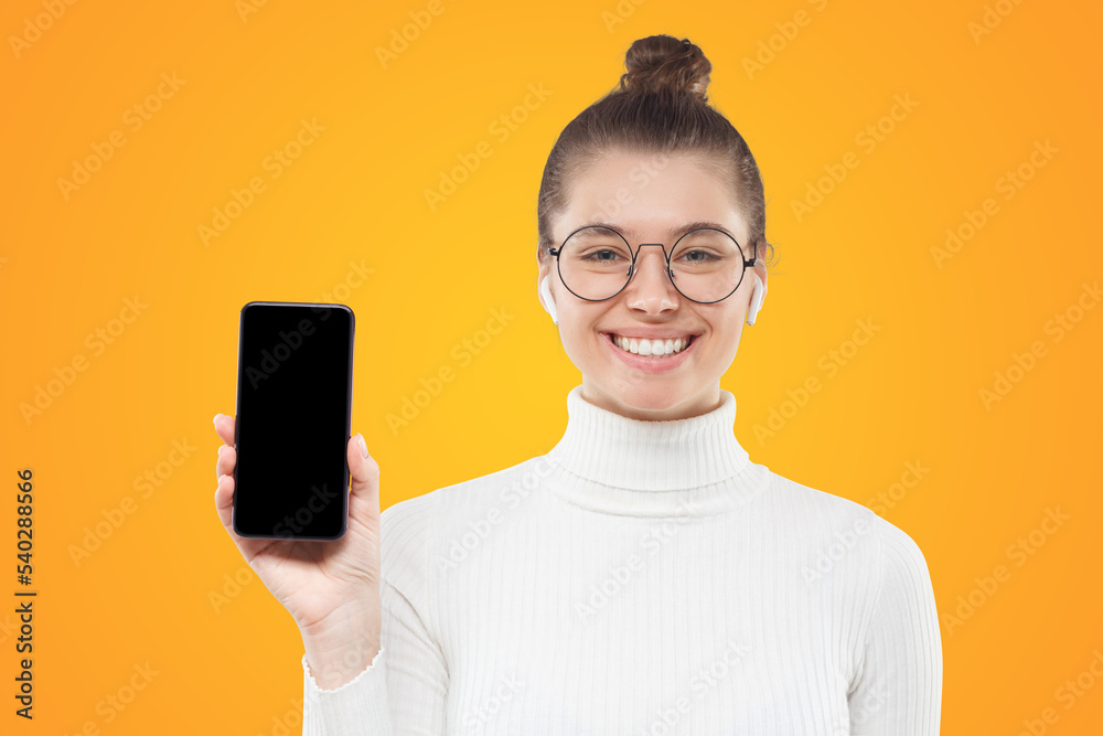 Young female in glasses showing smartphone with blank screen copy space to viewer
