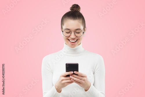 Young female in round glasses feeling relaxed and happy, laughing at funny content on phone screen © Damir Khabirov