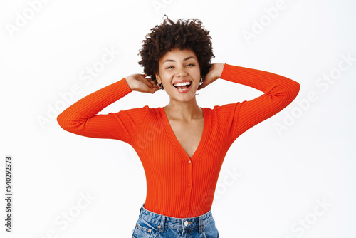 Carefree woman touches her new haircut, smiles and looks happy, stands over white background
