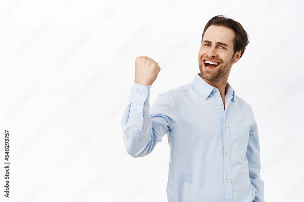 Handsome triumphing man fist pump, celebrating victory or achievement, smiling pleased, standing over white background Handsome triumphing man fist pump, celebrating victory or achievement, smiling pleased, standing over white background