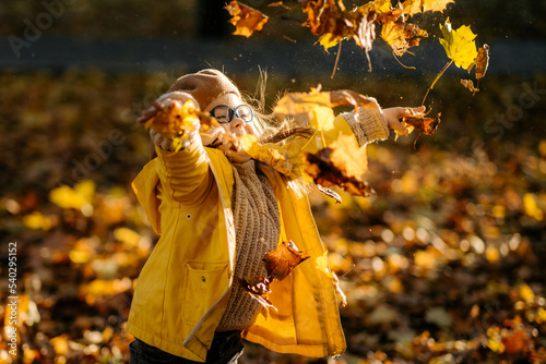 Happy child with down syndrome enjoying autumn day in the park tossing autumn leaves