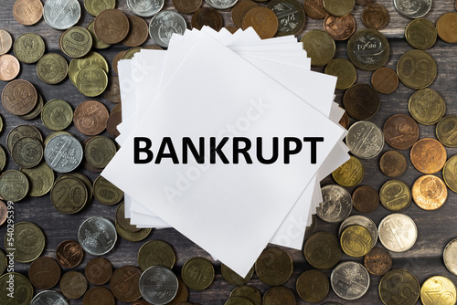 The inscription is bankrupt on a white sheet. Background of coins. The concept of economic crisis and sanctions