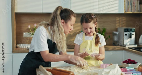 Beautiful young blonde older sister teaching little one kneading dough in modenr light kitchen. Happy girls cooking baking pizza pasta gnocchi preparing tasty delisiouc family dinner . photo