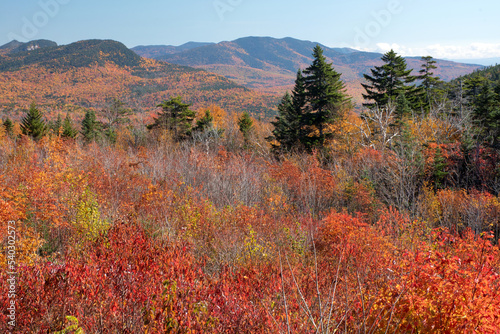 Stunning view of vibrant fall foliage and distant mountains in White Mountain National Forest from scenic overlook along New Hampshire’s Kancamagus Highway.