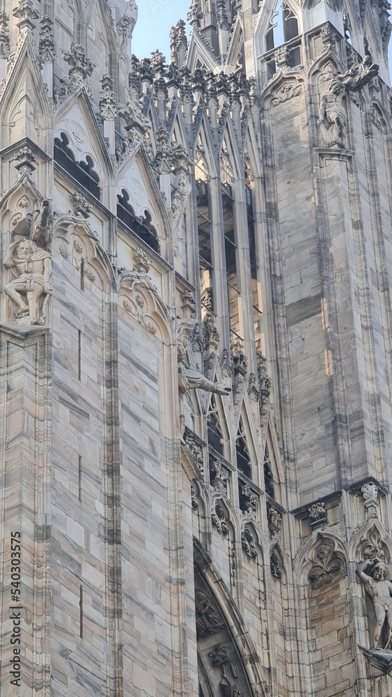 Obraz premium Milan Italy- October 17, 2022: Milan cathedral Duomo di Milano with gothic spires and white marble statues. Top tourist attraction on piazza in Milan, wide angle view of old gothic architecture.