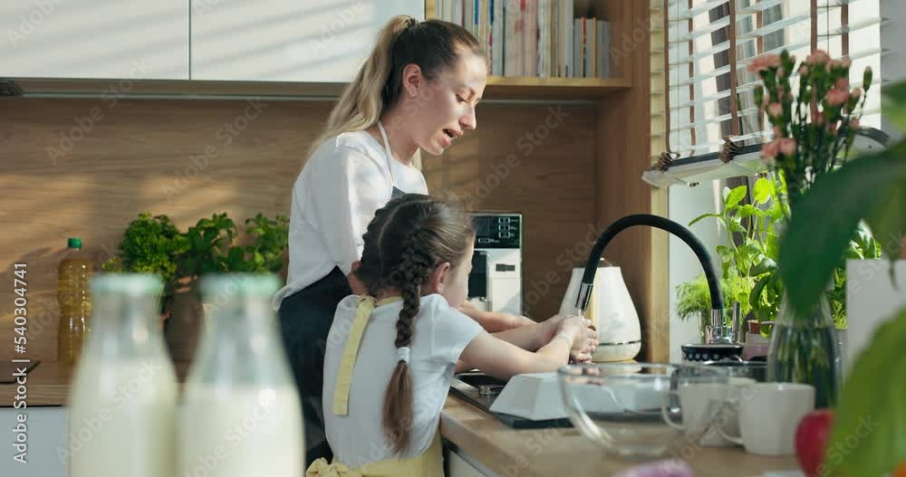 Young beautiful mother with preschooler daughter in aprons washing hands playing with water preparing hands for cooking baking tsty cookies delicious biscuits pizza pasta .