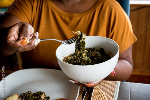 Black woman holding bowl and fork full of collard greens during Sunday dinner, soul food