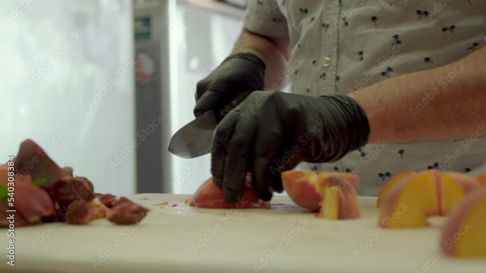 Man slicing juicy peaches wearing black gloves