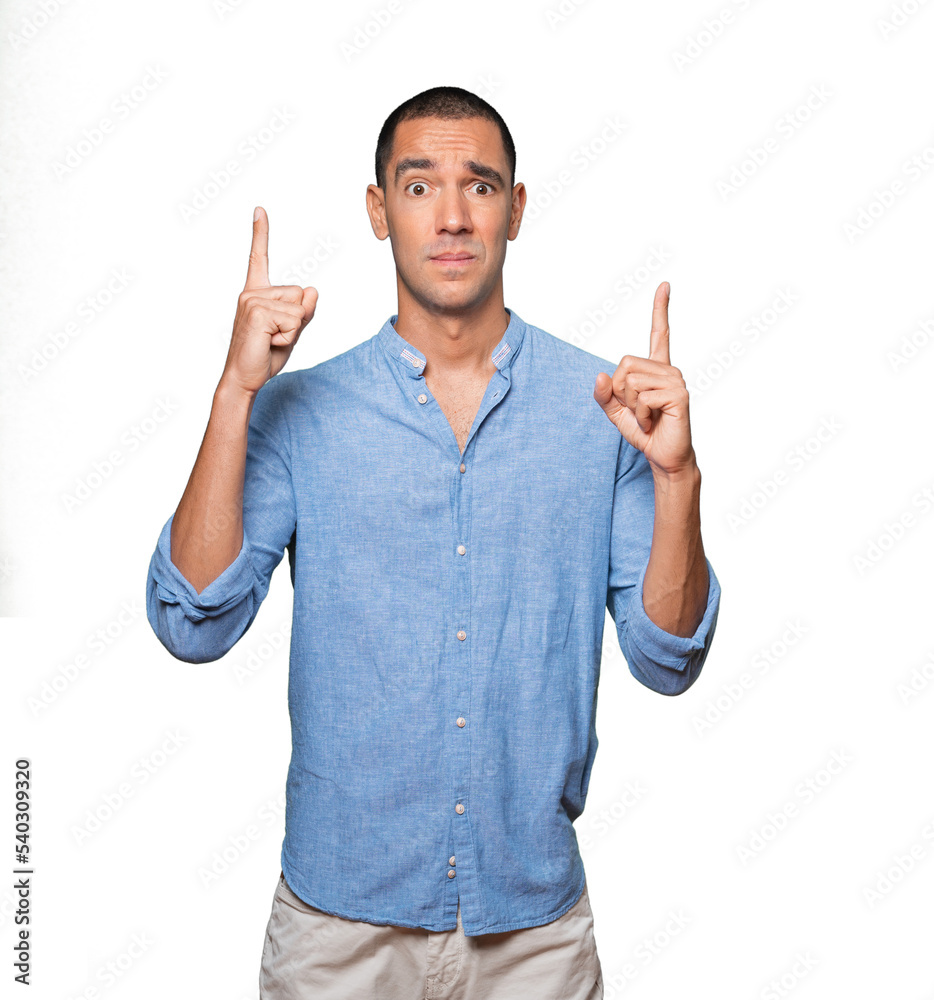 Hesitant young man pointing up with his finger Hesitant young man pointing up with his finger