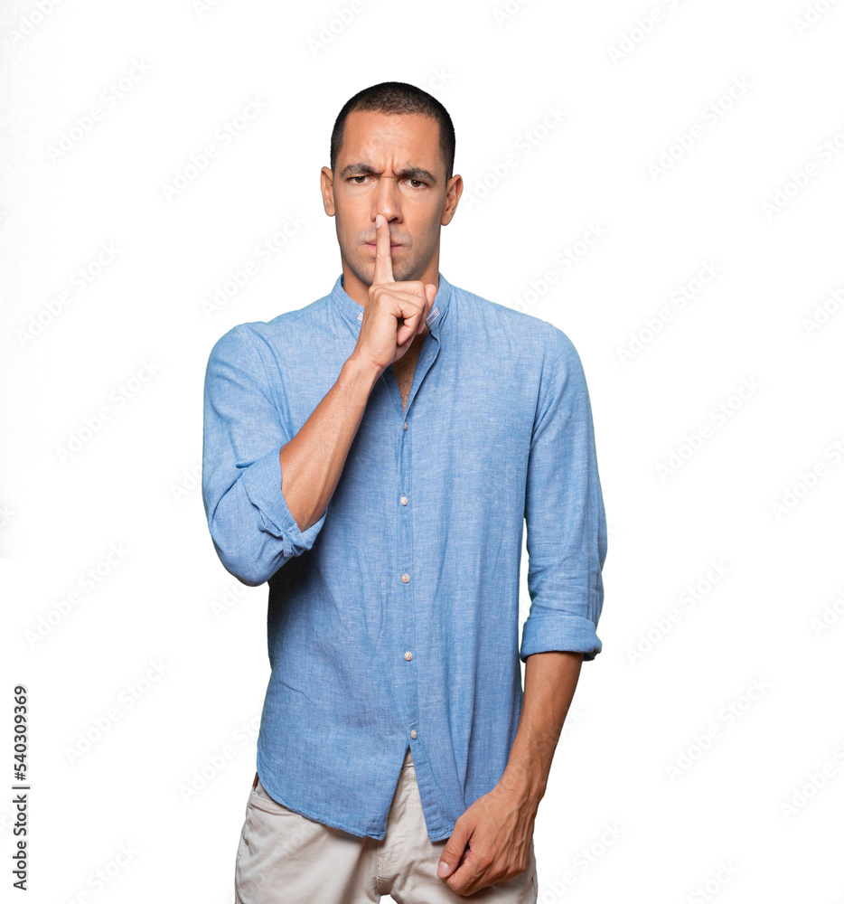Serious young man asking for silence gesturing with his finger Serious young man asking for silence gesturing with his finger