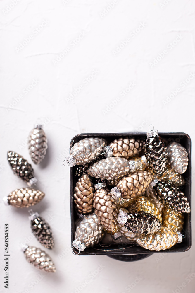 Fototapeta premium Christmas decorations. Metallic box with glass gold, black, silver decorative cones on white textured background. Scandinavian minimalistic style. Still life. Place for text.