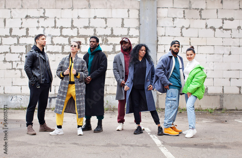 Canvas Print Multiethnic group of young hipsters stands together on street against gray brick wall