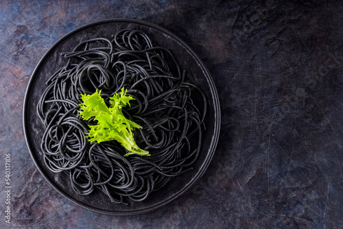 Black spaghetti with cuttlefish ink on a dark background. Cooked black spaghetti pasta with green lettuce. Top view. Copy space