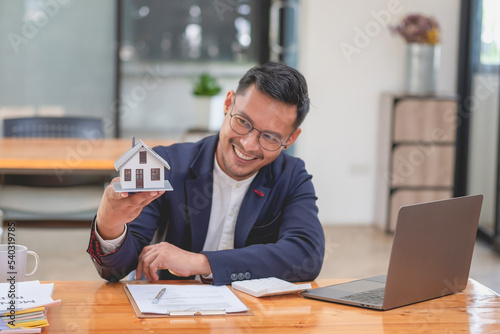 Accountant, businessman, real estate agent, businessman handing model house to customers along with house interest calculation documents for customers to sign.