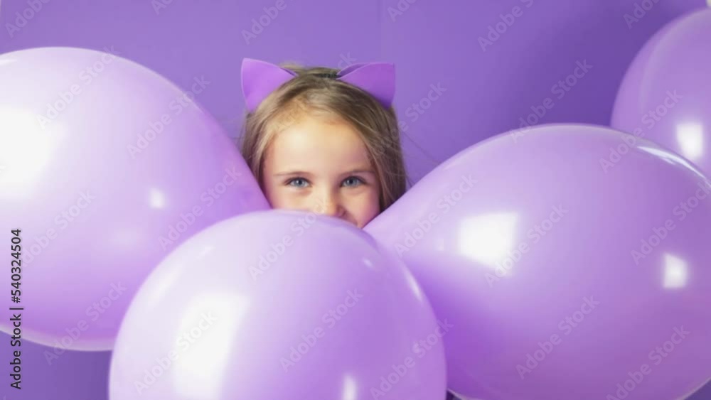 Gorgeous little girl with cat ears, balloons on a purple background. Halloween concept Gorgeous little girl with cat ears, balloons on a purple background. Halloween concept