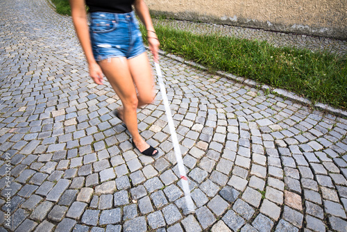 Blind woman walking on city streets, using her white cane to navigate the urban space better and to get to her destination safely photo