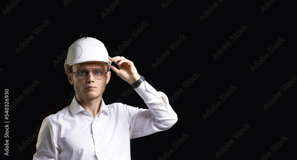 portrait of a young male engineer designer architect in business clothes and a hard hat on a dark background. portrait of a young male engineer designer architect in business clothes and a hard hat on a dark background.