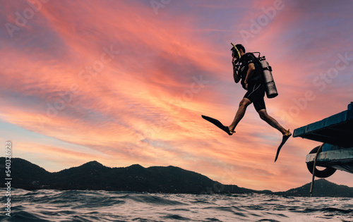 Scuba Diver Jumping to the open ocean on a background sunset doing giant jump