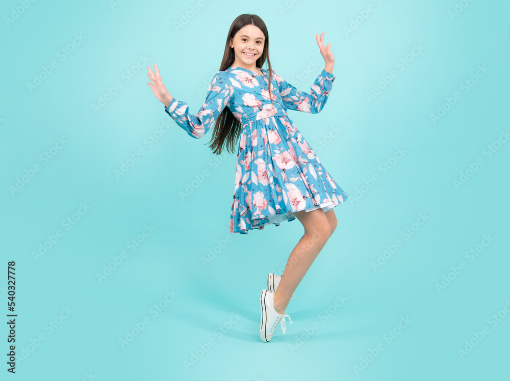 Full length cheerful teenager kid jump enjoy rejoice win isolated on blue background. Small child girl in summer dress jumping Full length cheerful teenager kid jump enjoy rejoice win isolated on blue background. Small child girl in summer dress jumping