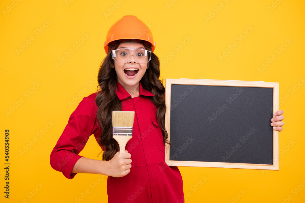 Excited teenager girl painter in helmet with painting brush. Blackboard for copy space. Child in hard hat. Kid builder painter on construction site. Renovation and repair. Excited teenager girl painter in helmet with painting brush. Blackboard for copy space. Child in hard hat. Kid builder painter on construction site. Renovation and repair.