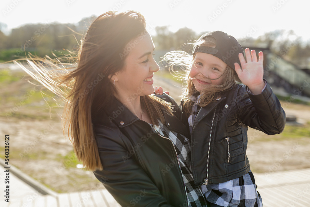 Fototapeta premium Close up portrait of happy little adorable girl smiling, having fun and waiving ay camera while spending time with her mother outdoor in sunlight 