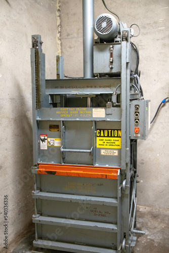 Grey steel industrial paper baler in a concrete corridor, nobody