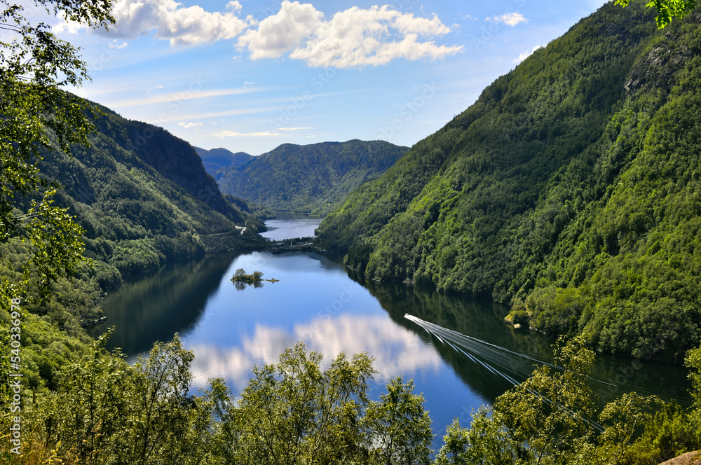Fjord in Norway with forested mountains, deep valley and water with ship and island.