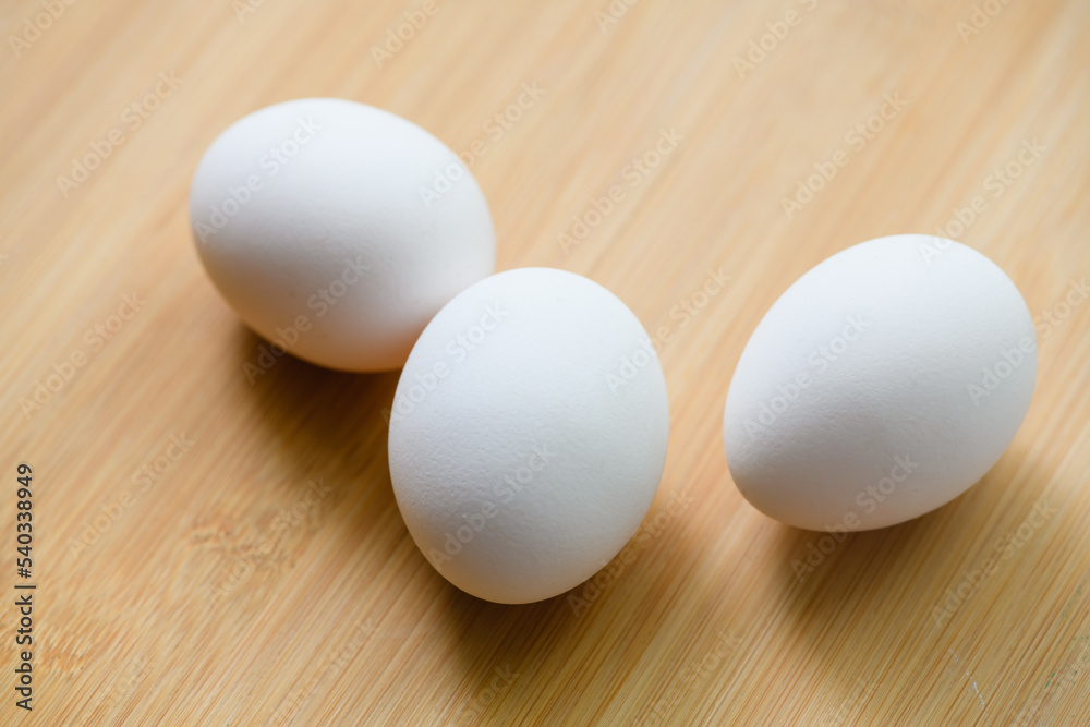Three chicken eggs on a cutting board, close-up. Three chicken eggs on a cutting board, close-up.