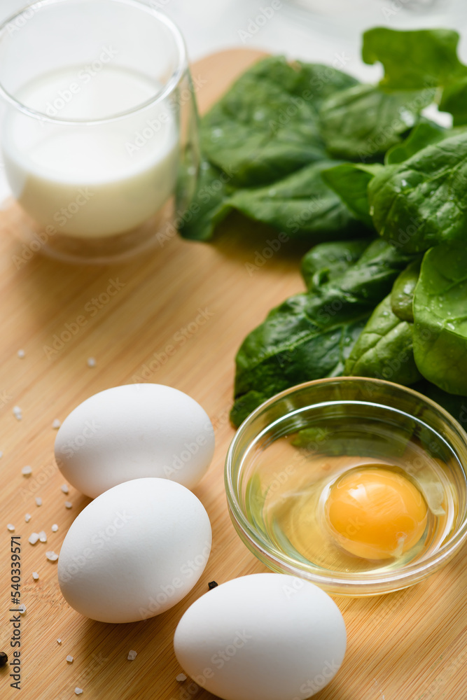 White chicken eggs on a cutting board with a bunch of fresh spinach.
