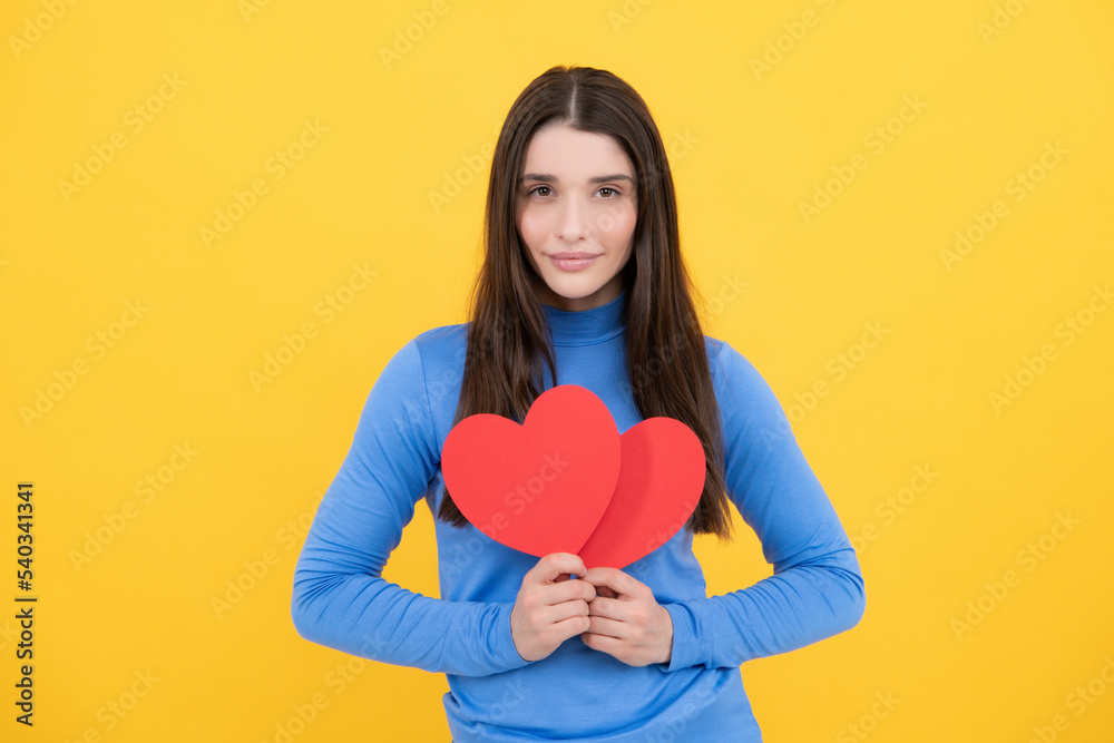 Happy woman hold red heart. Beautiful female model posing on isolated yellow background. Cheerful positive cute pretty tender girl with heart. Happy woman hold red heart. Beautiful female model posing on isolated yellow background. Cheerful positive cute pretty tender girl with heart.