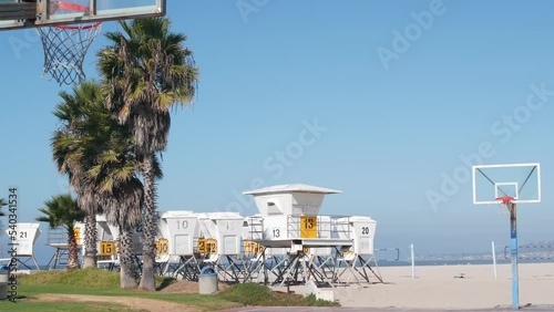 Palm trees and basketball sport field or court on beach, California coast, USA. Streetball playground on shore and lifeguard stand, tower ot station. Mission beach, San Diego. Hoop, backboard and sky.