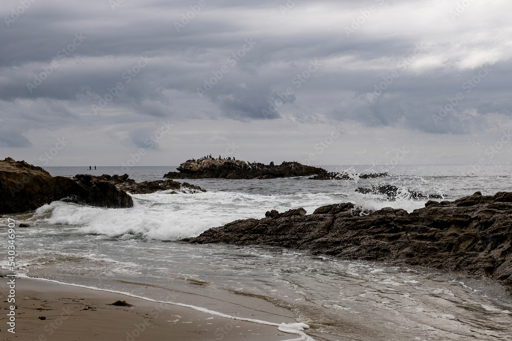 Bird Rock and waves crashing on the shore rocks of Laguna Beach, California on a cloudy day.