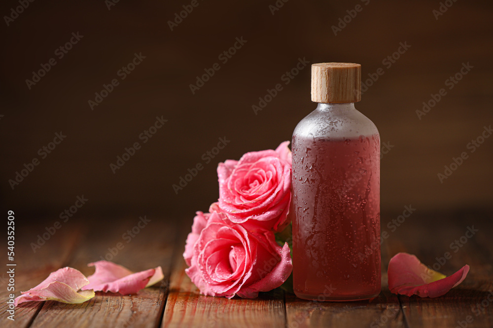Bottle of essential rose oil and flowers on wooden table, space for text Bottle of essential rose oil and flowers on wooden table, space for text