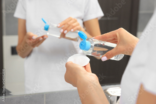 Woman pouring micellar water onto cotton pad in bathroom, closeup