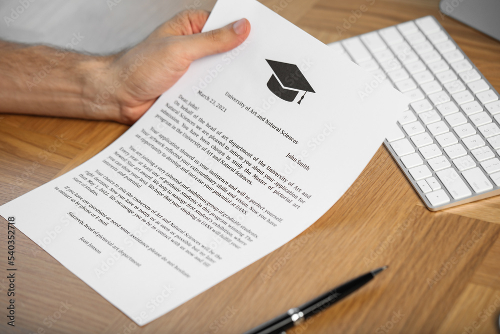 Obraz premium Student with acceptance letter from university at wooden table indoors, closeup